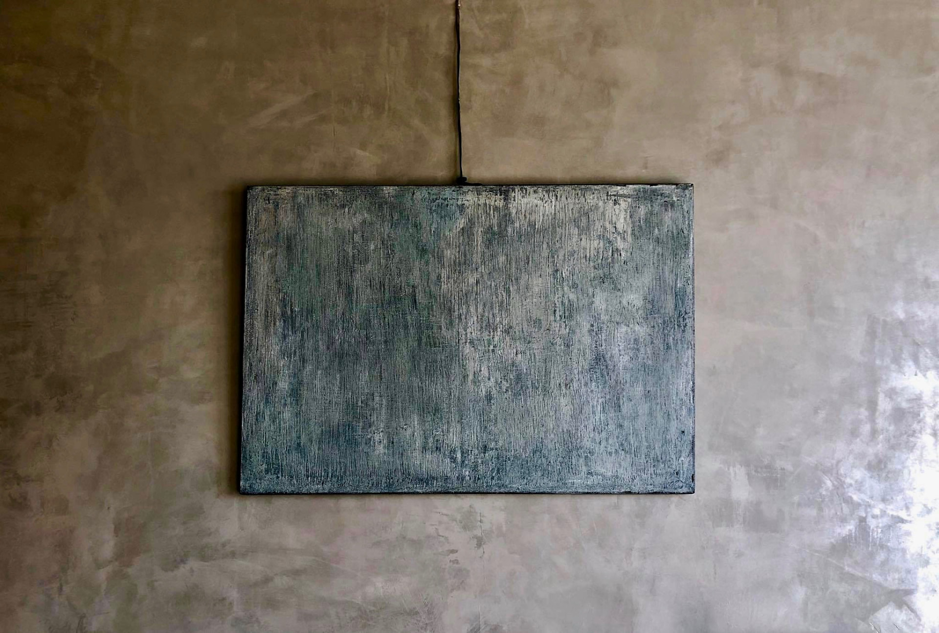 Blue-grey textured painting hung on a warm plaster wall